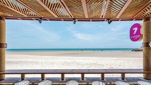 Une vue sur la plage depuis un espace abrité, doté d’un plafond en bois et d’un panneau indiquant « A SEVEN ».