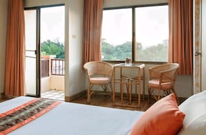 A hotel room with a bed, two wicker chairs, a small table, and a balcony with curtains.