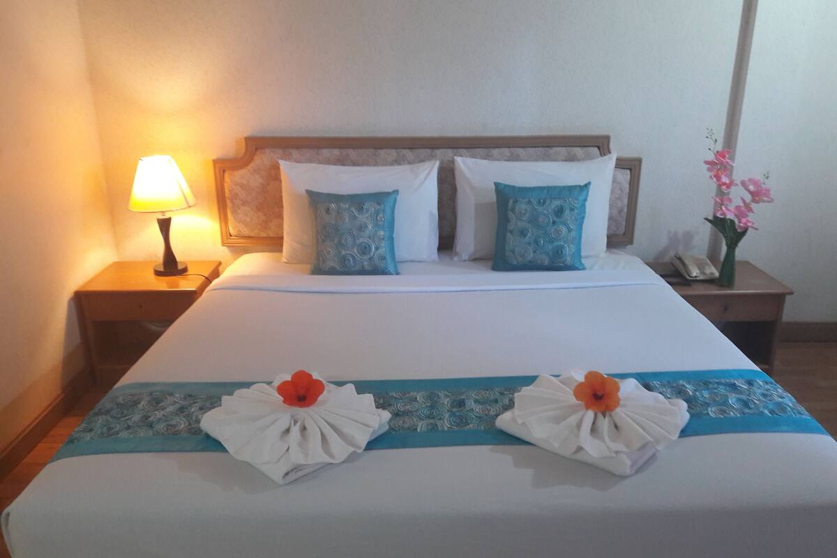 Un lit bien fait, recouvert d’une couvre-lit bleue et blanche, avec deux serviettes décoratives et une lampe de chevet.