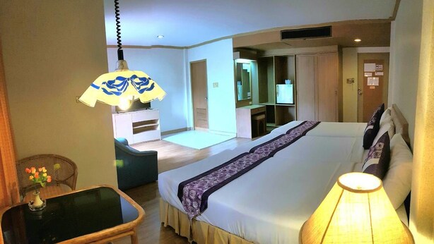 A hotel room with a bed, bedside table, lamp, and a small table with flowers. - Takiab Beach Resort (Hua Hin)