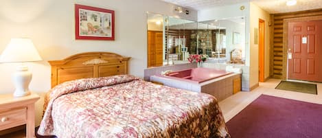 A bedroom with a bed, a nightstand, a dresser, a mirror, a bathroom with a bathtub, and a door.