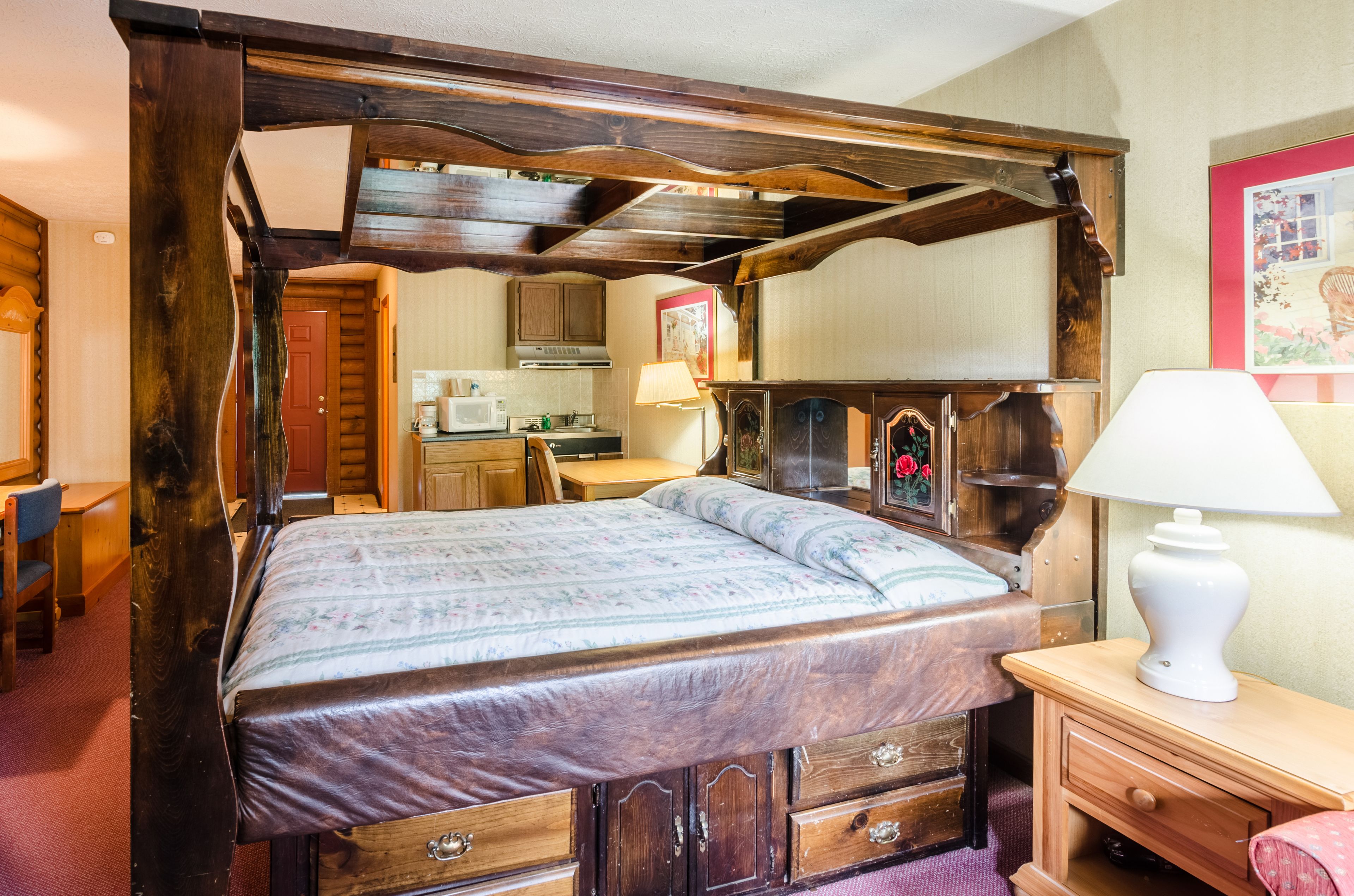 Ein traditionelles Himmelbett mit Holz Kopfteil, ein Nachttisch mit Lampe und ein kleiner Schrank.