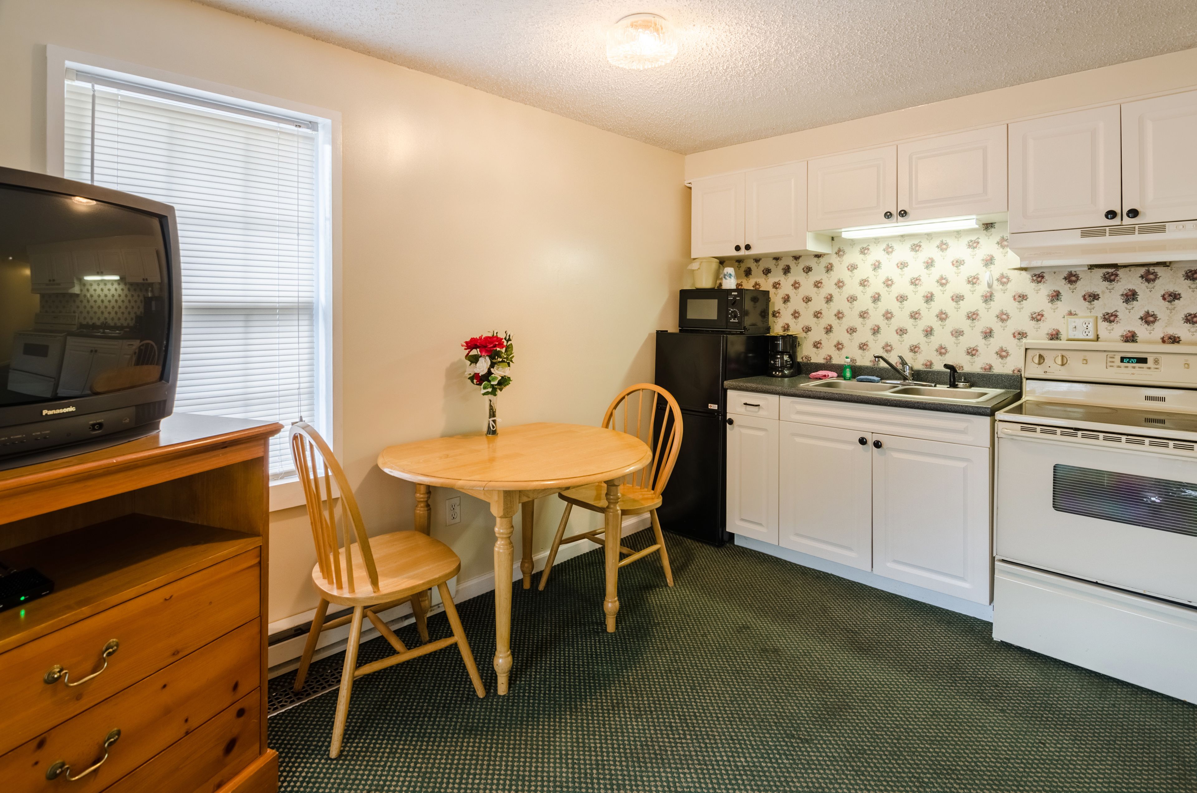 Una cocina compacta con muebles blancos, un microondas, una estufa y una mesa de comedor de madera con sillas.