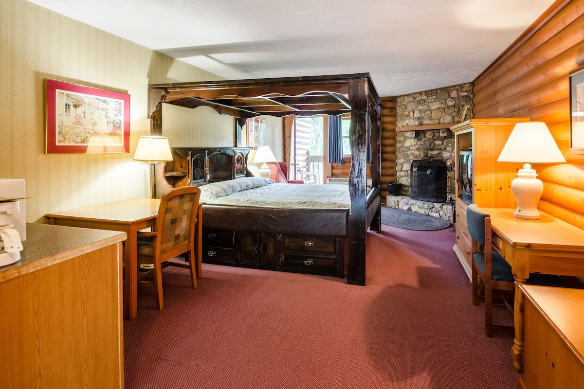 Un lit à baldaquin avec une cheminée en pierre, des meubles en bois et un tableau encadré au mur.