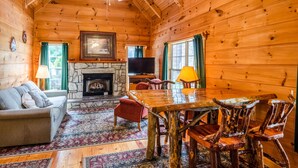 Ein Blockhaus-Interieur mit Kamin aus Naturstein, einem Holzespeisetisch und einem Fernseher.