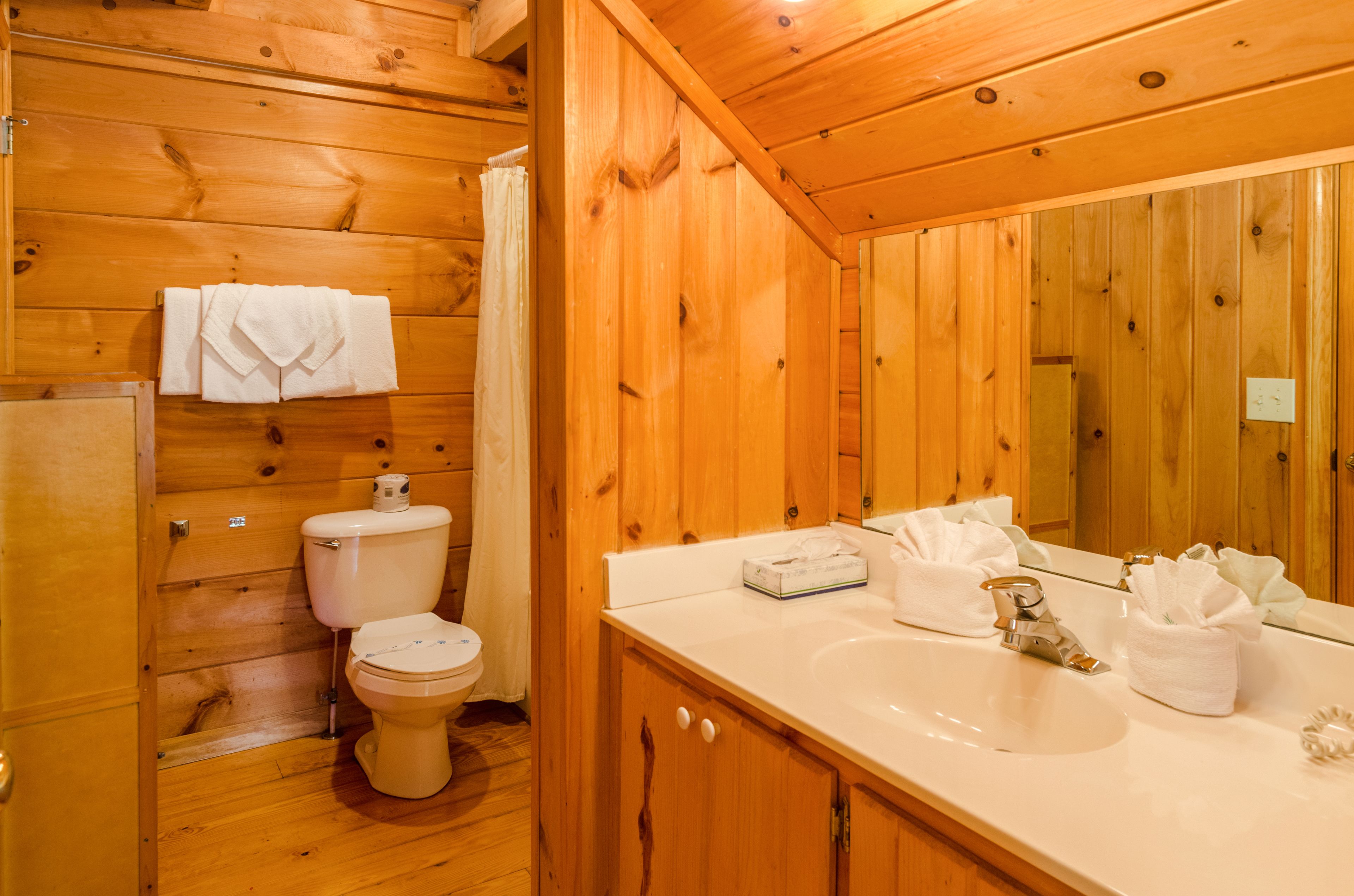 A wooden cabin bathroom with a toilet, sink, and mirror.