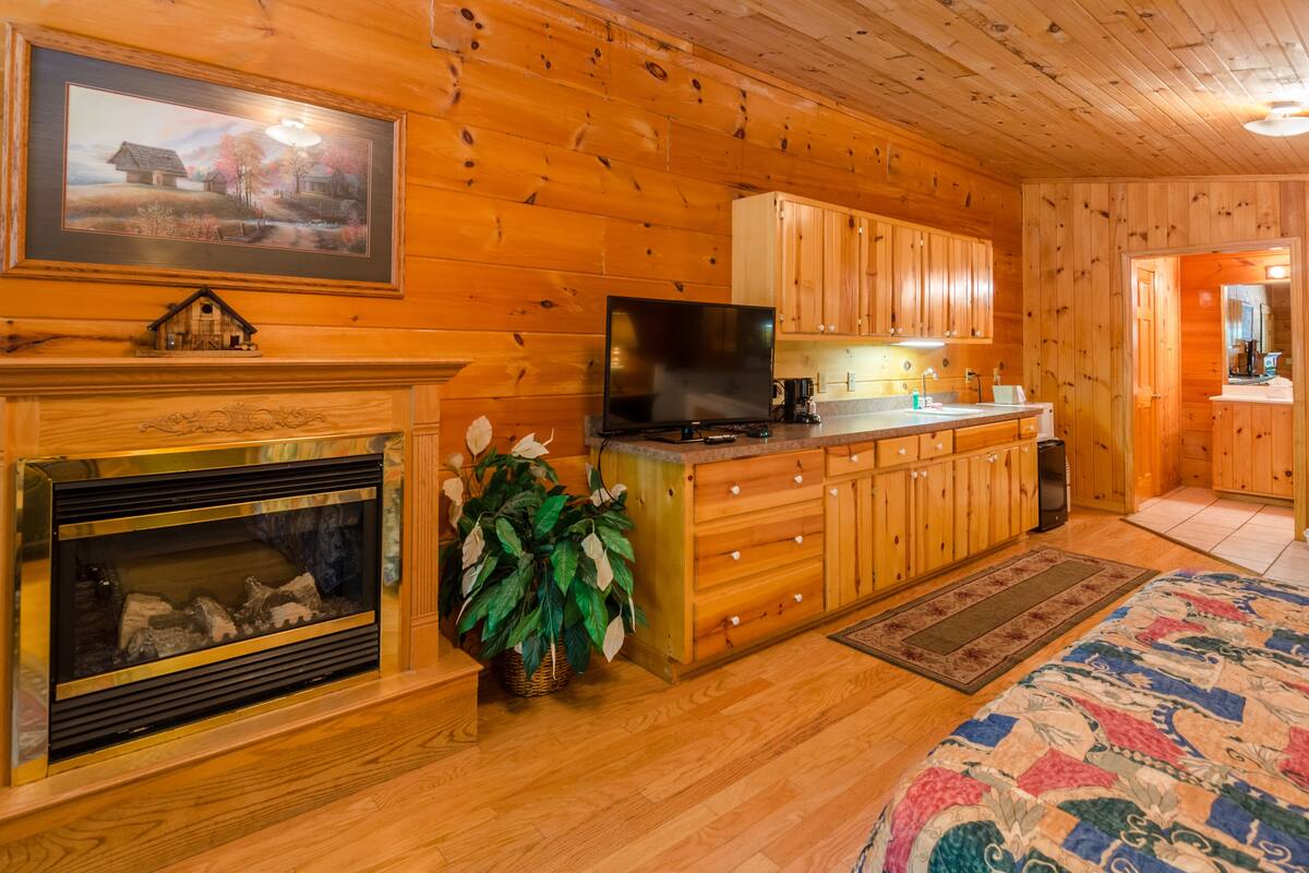 L’intérieur chaleureux d’un chalet avec une cheminée, des meubles en bois, un téléviseur et une courtepointe.