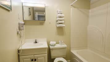 Un baño con lavamanos, inodoro y bañera. Hay toallas colgadas en la pared y un secador de pelo también.
