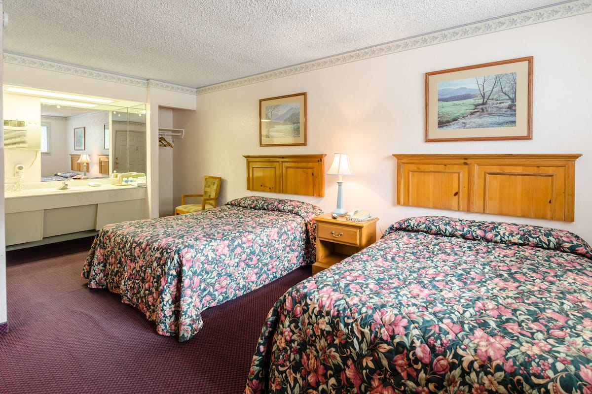 Une chambre d’hôtel avec deux lits, un grand miroir, une tête de lit en bois, une table de chevet avec une lampe et un tableau encadré au mur.