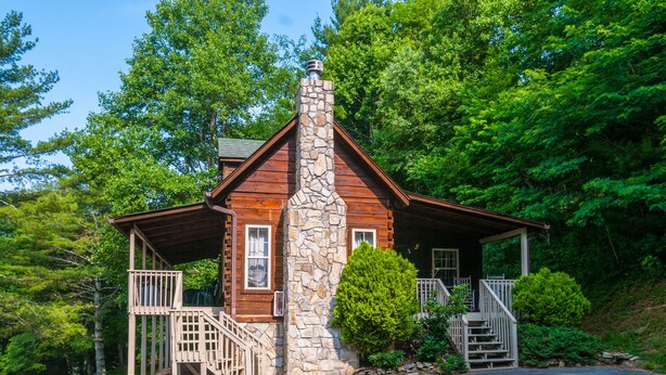 Eine Holzhütte mit Steinkamin, Holzfassade und einer Veranda mit Stufen zu einer Terrasse.