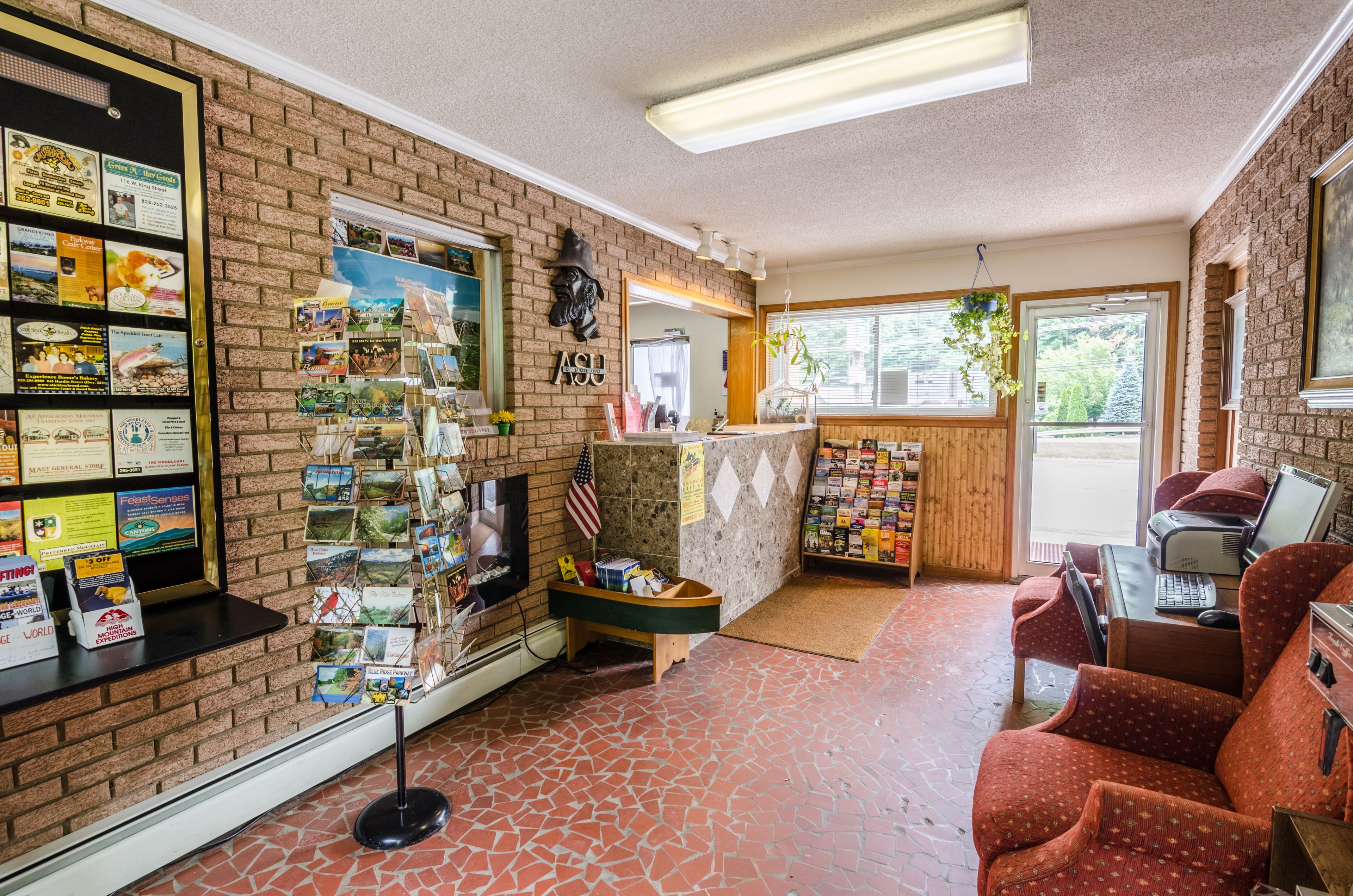 Eine Lobby mit Ziegelwand, Empfangstresen, Computer, Kamin und einer roten Couch.
