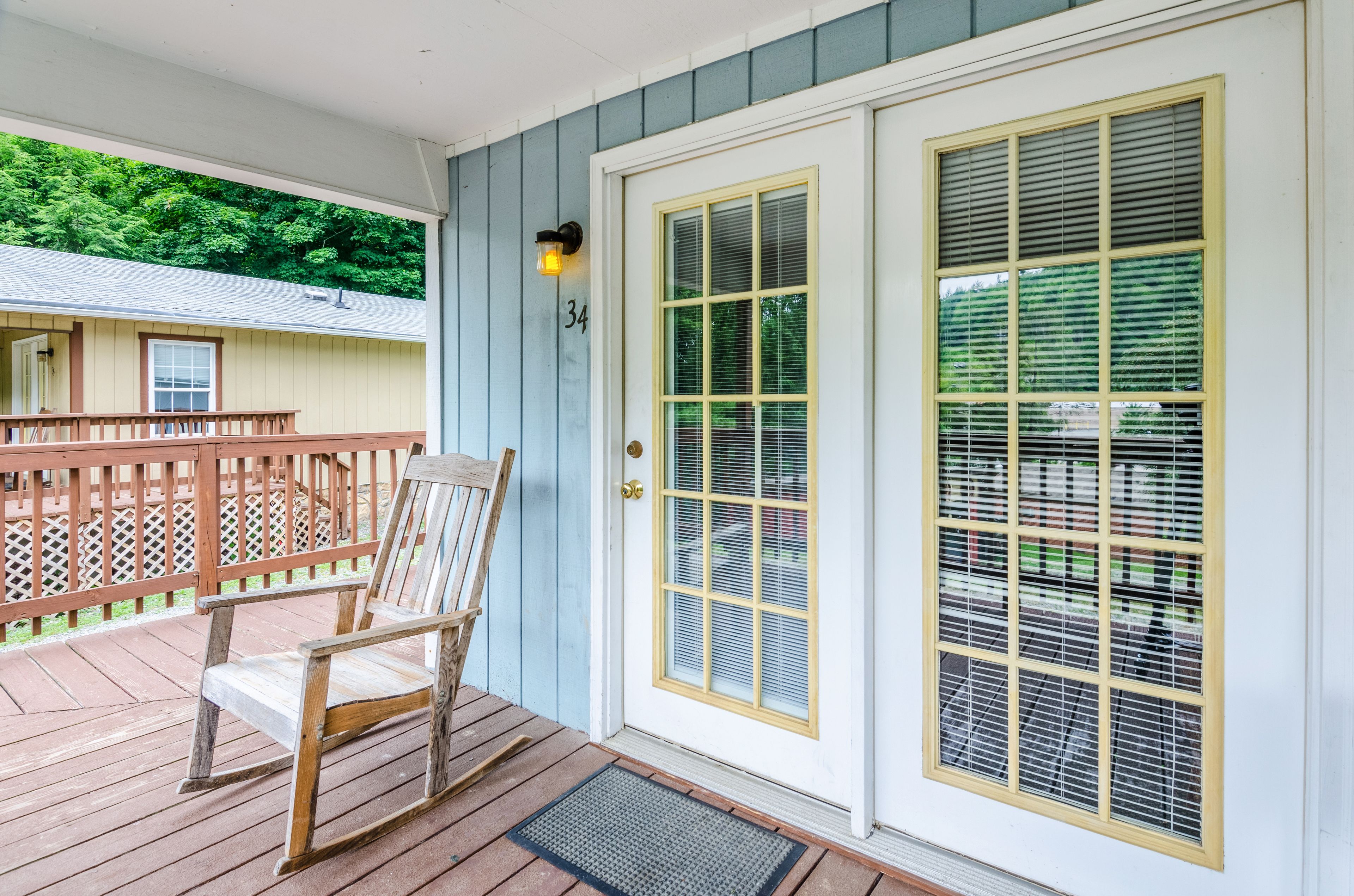 A wooden deck with a chair, a door with a number, and a window with blinds.