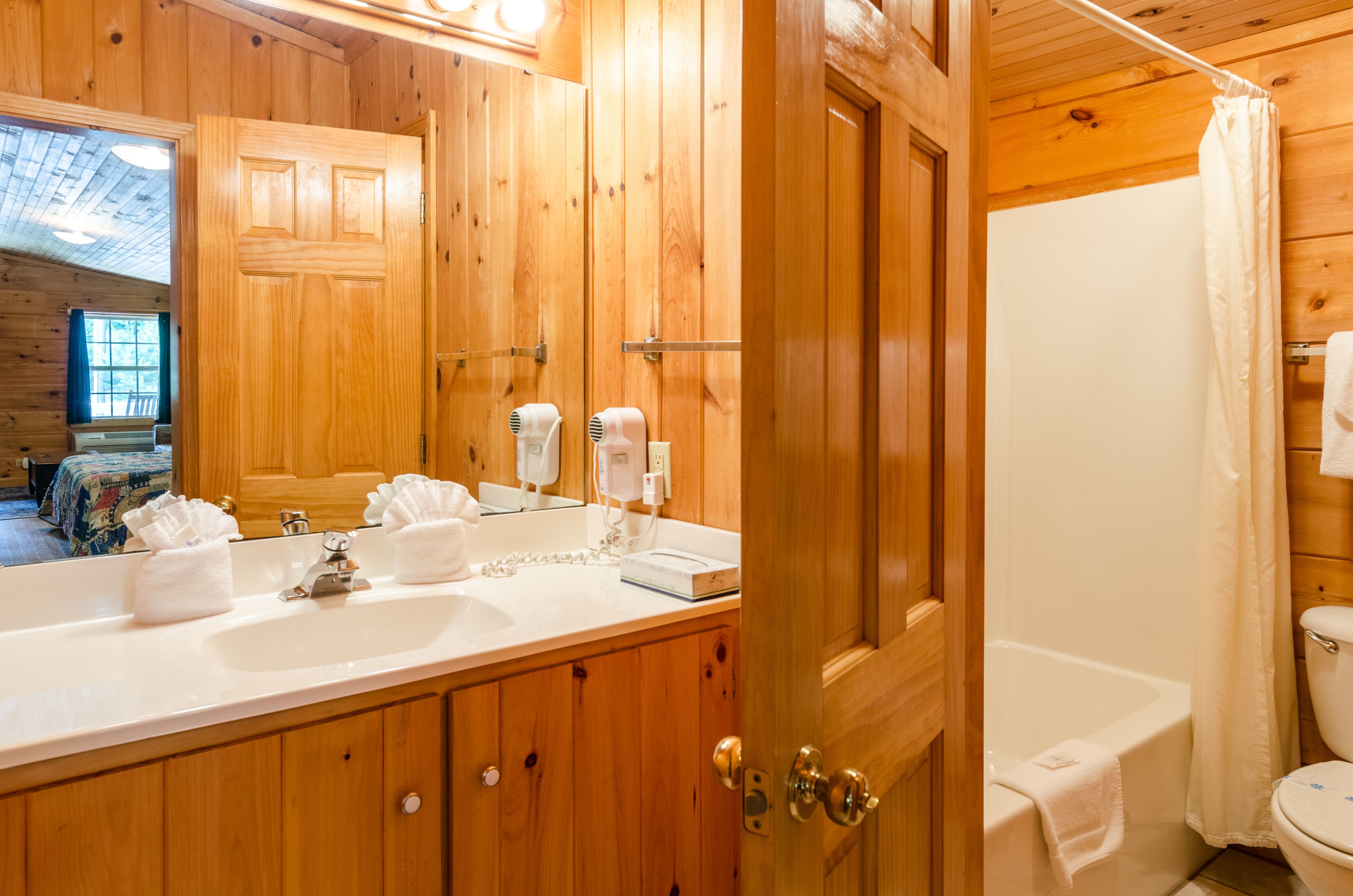 A wooden bathroom with a large mirror, two sinks, and a bathtub.