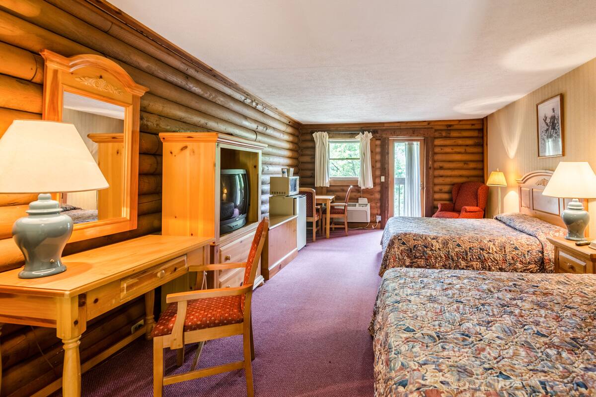 Une chambre de style rustique avec deux lits, un bureau, une chaise, une télévision et une fenêtre.
