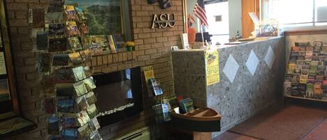 Zona de recepción con pared de ladrillo, una bandera estadounidense colgada, una gran exhibición de postales y un mostrador con diversos artículos.