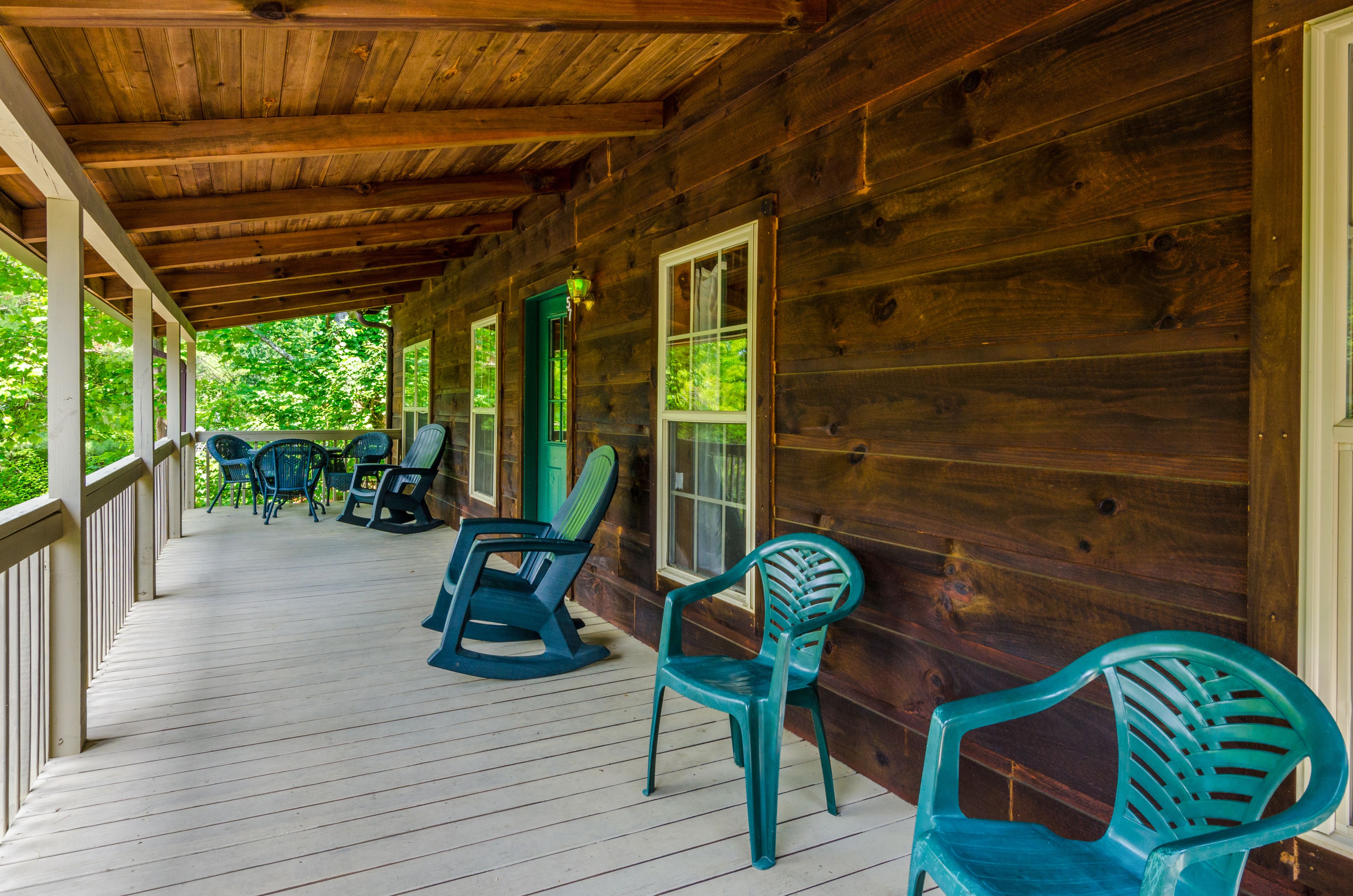 A wooden porch with several chairs and a table, surrounded by a wooden fence.