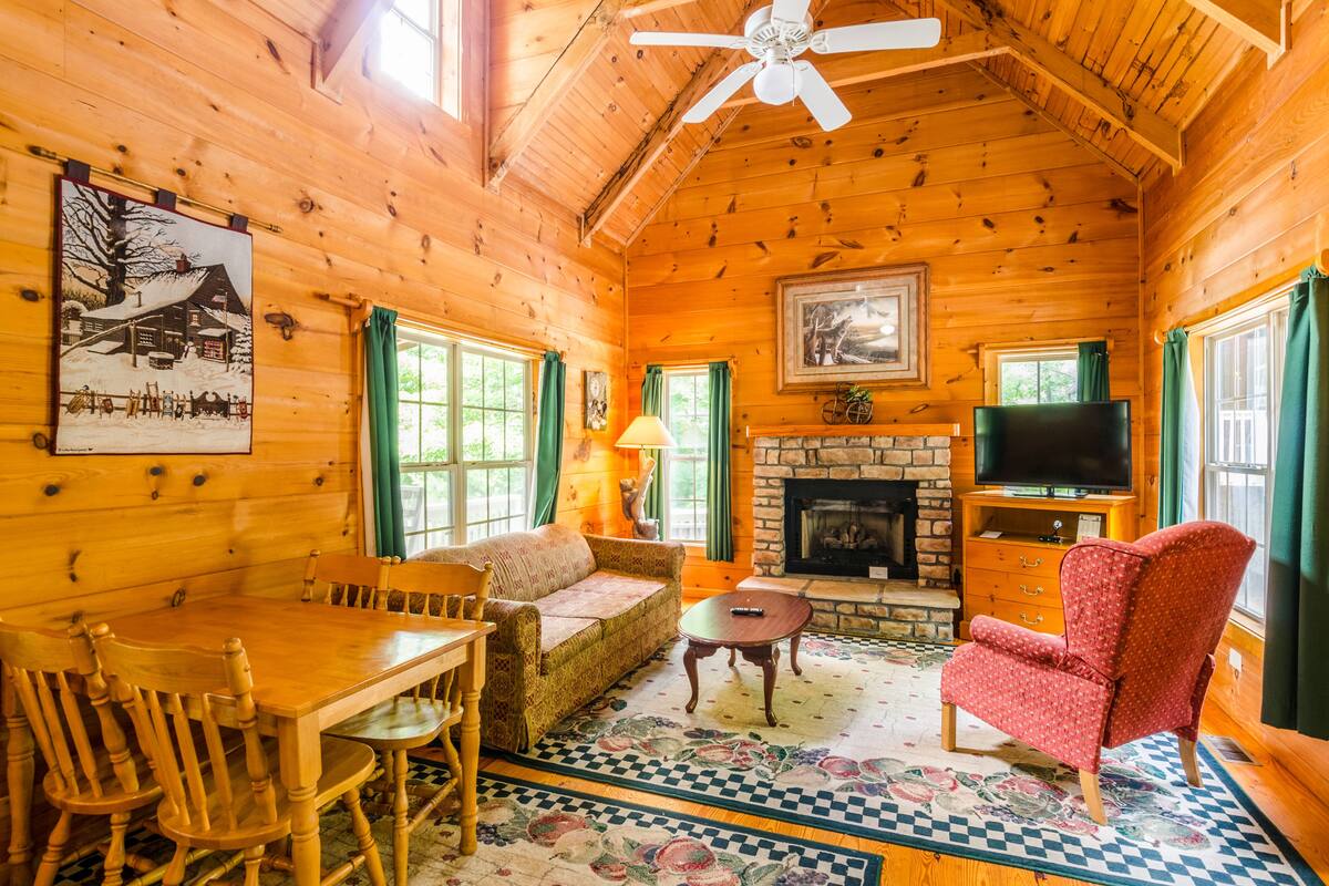 L’intérieur d’un chalet confortable, avec une cheminée, des meubles en bois et un téléviseur.