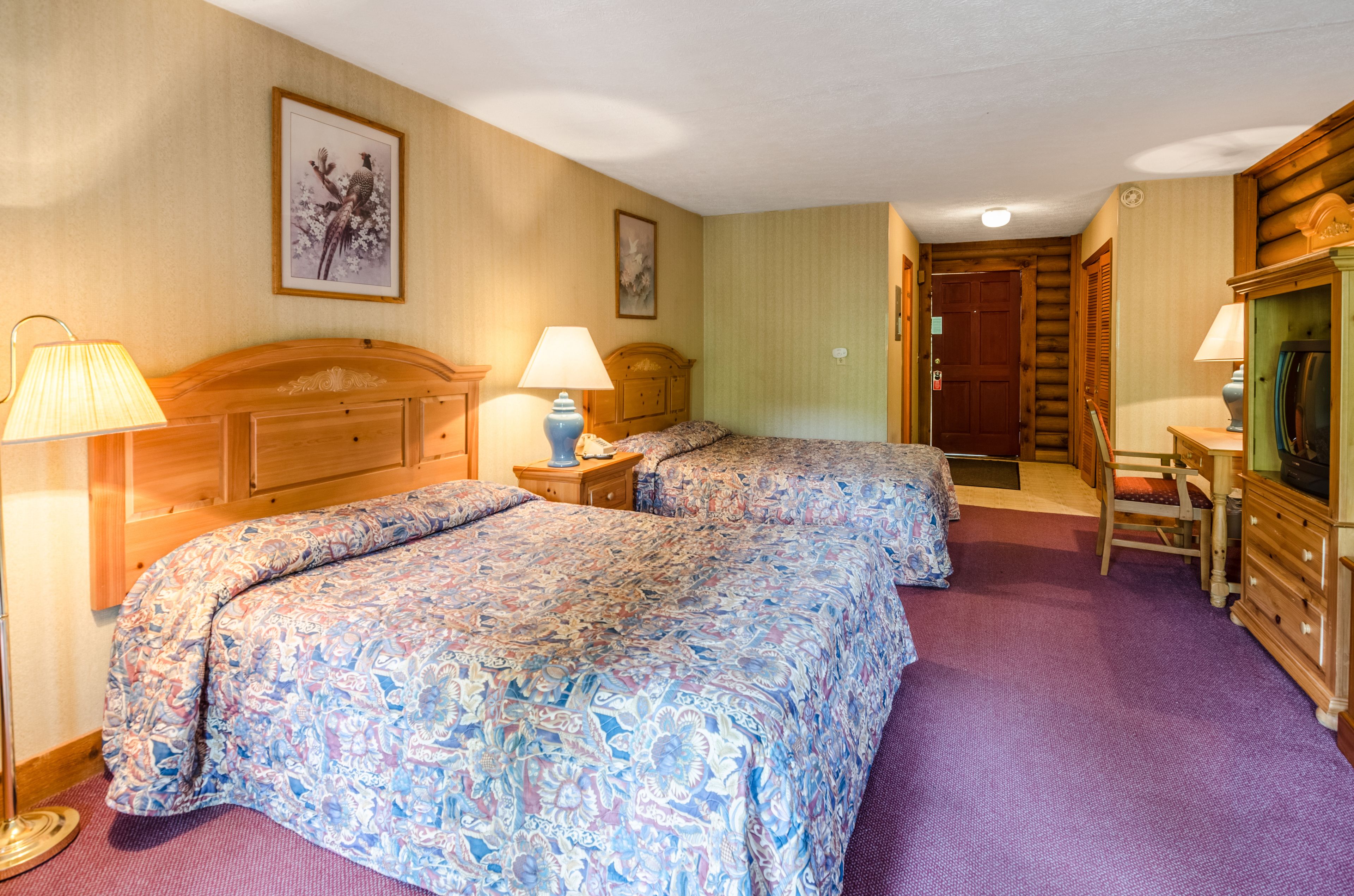 Ein Hotelzimmer mit zwei Betten, einem Holzkopfteil, einem Schreibtisch mit Stuhl und einer Lampe.