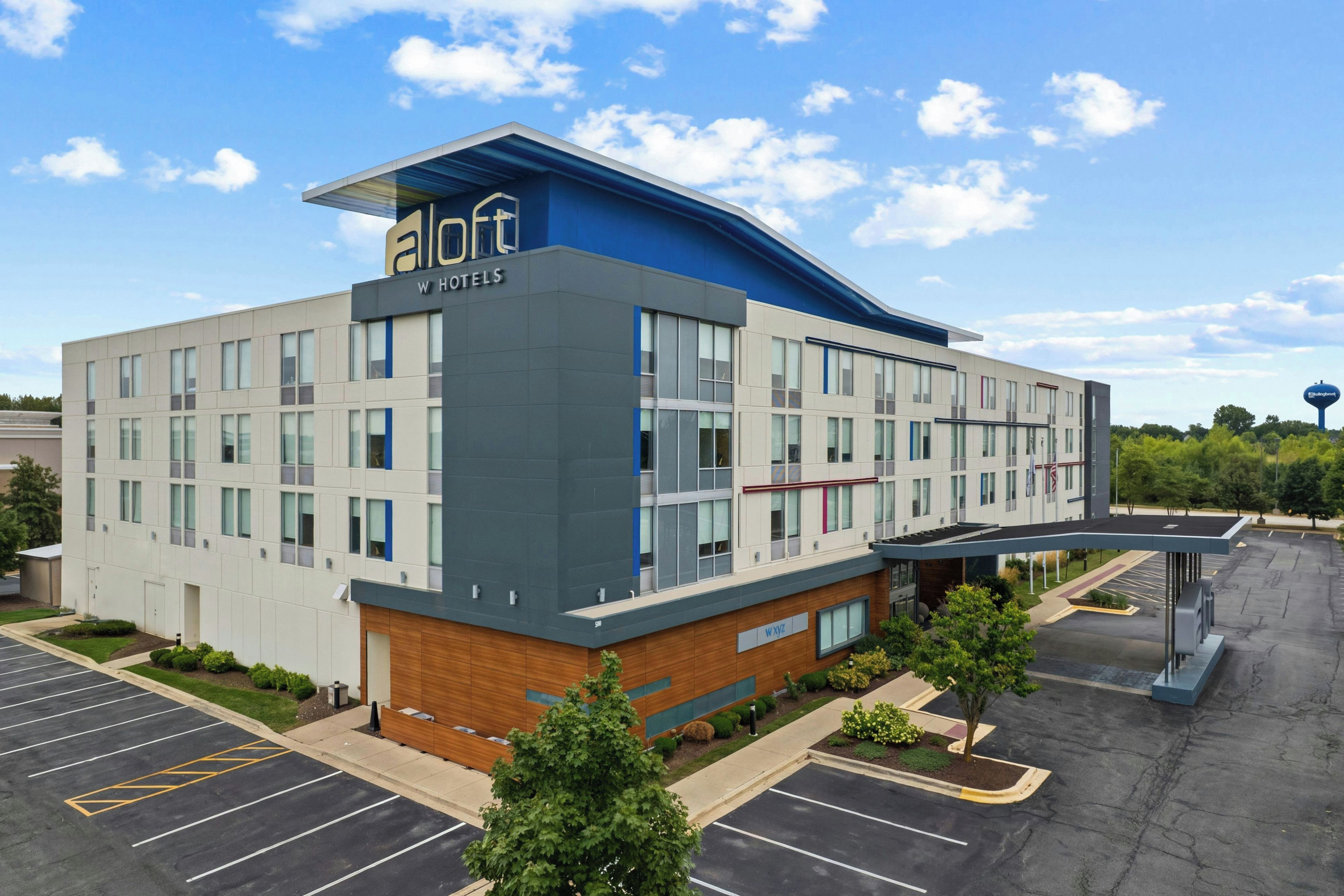 A modern hotel building with a flat roof, multiple windows, and a parking lot.