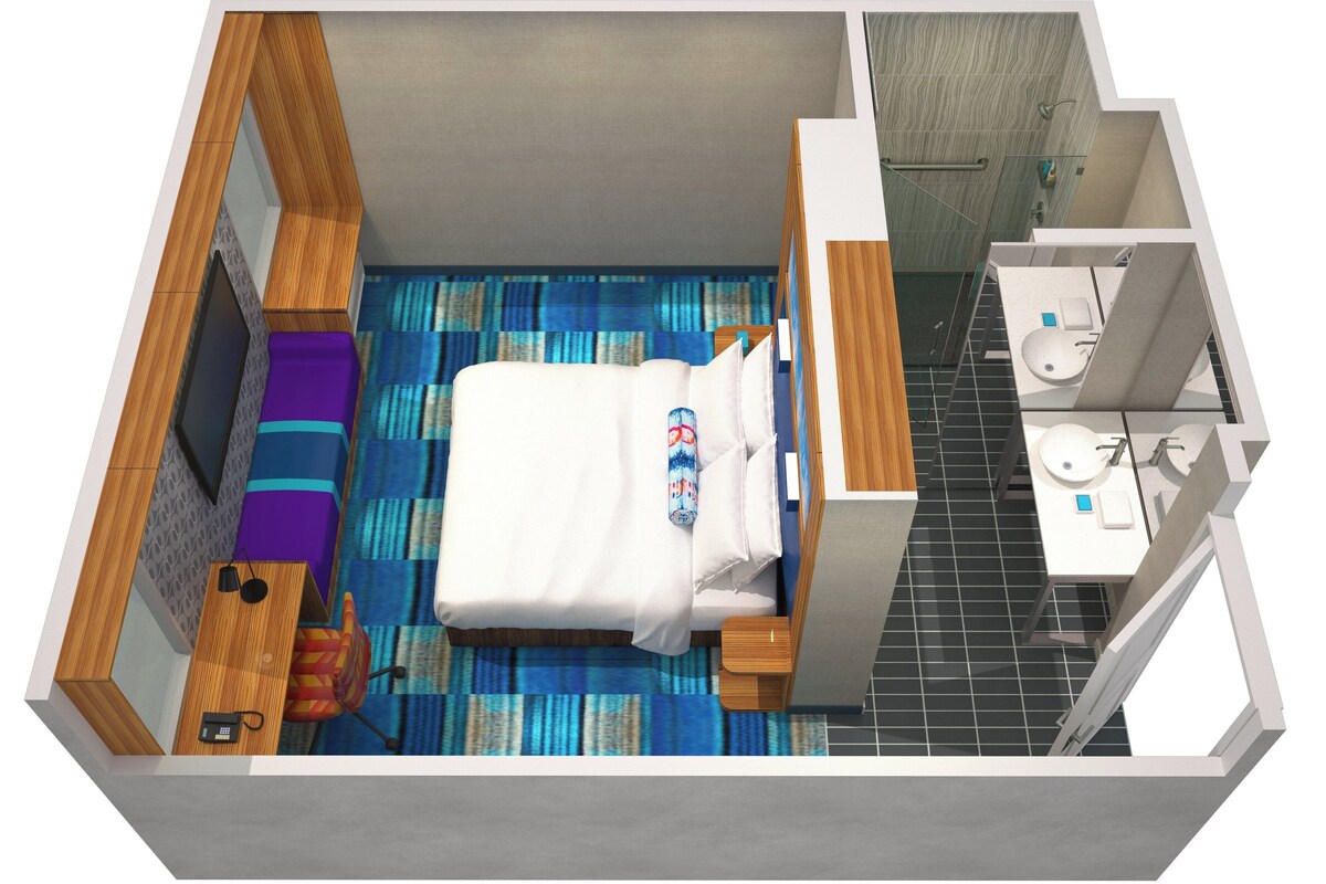A hotel room with a bed, a small desk, a chair, a bathroom with a sink and toilet, and a shower area.