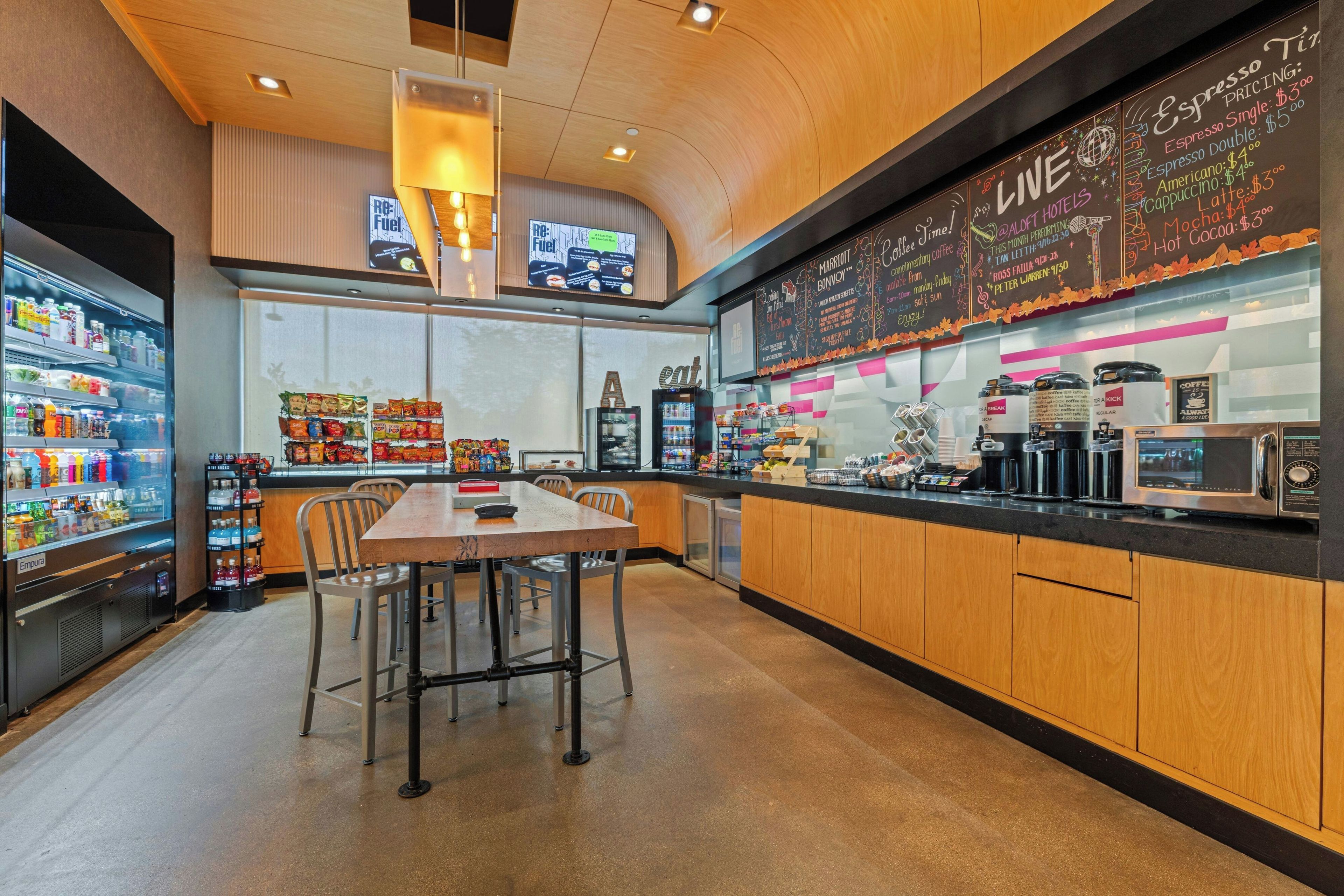 A coffee shop interior with a counter, seating area, and a refrigerator stocked with beverages.