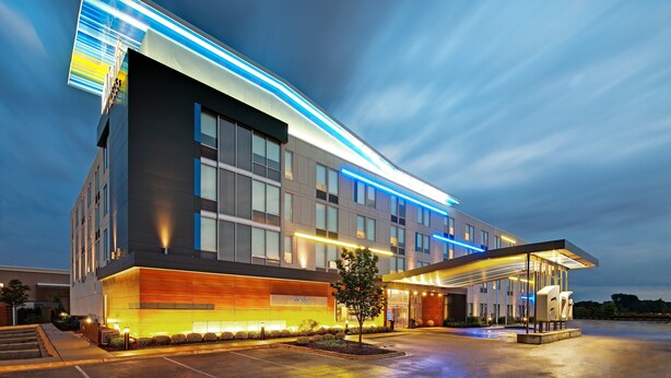 Un hotel moderno con un amplio frente de vidrio, una entrada cubierta y un área de estacionamiento bien iluminada.