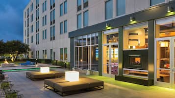 A modern hotel exterior with outdoor seating, large windows, and a visible bar area.