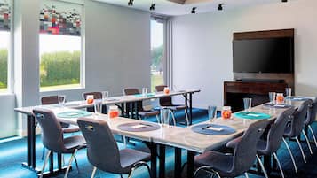 A conference room with a long table, chairs, a television, and a large window.
