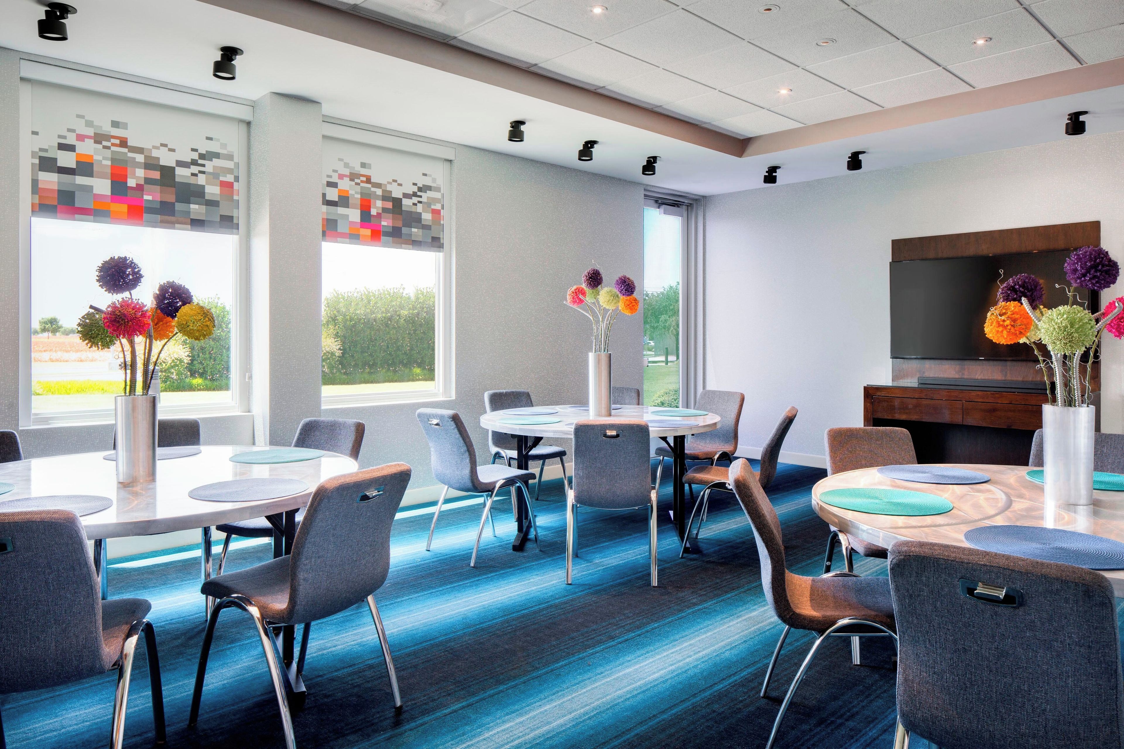 Un espace repas moderne avec des tables rondes, des chaises et un téléviseur à écran plat fixé au mur.