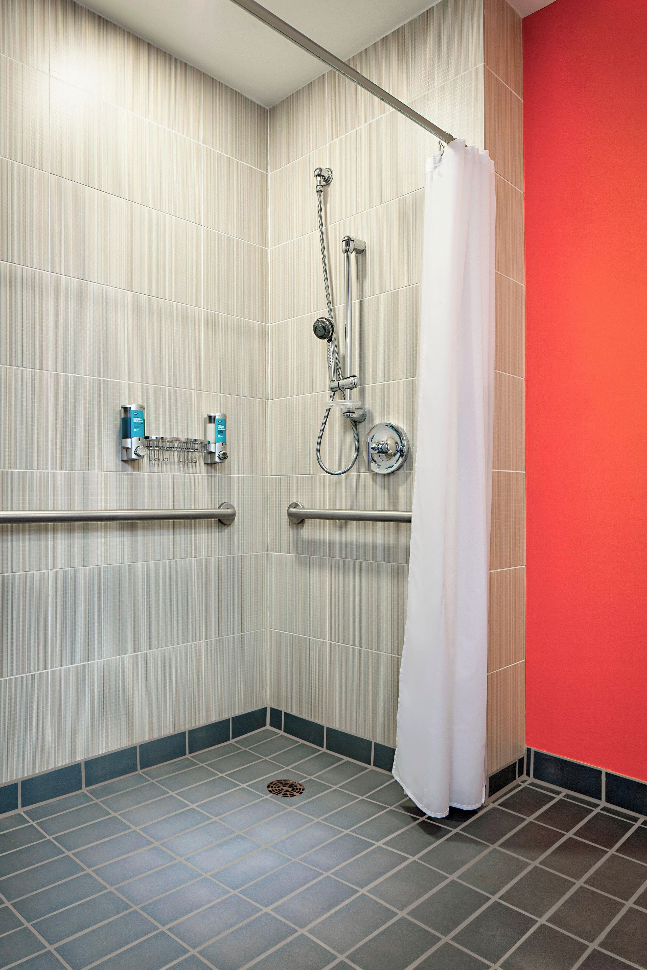 Een badkamer met een douche, grepen en een betegelde vloer.