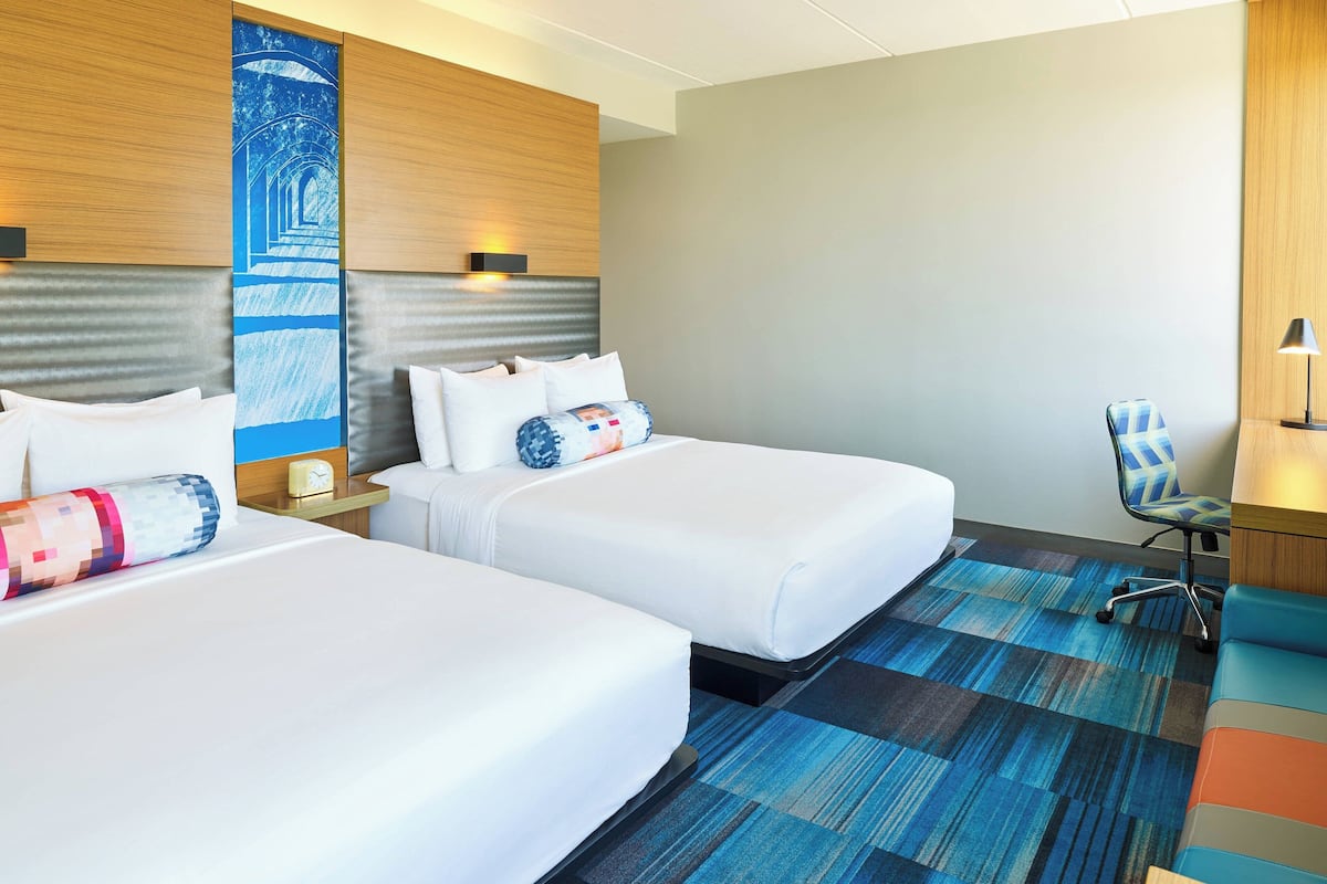 A hotel room with two beds, a blue patterned carpet, a wooden headboard, and a chair.