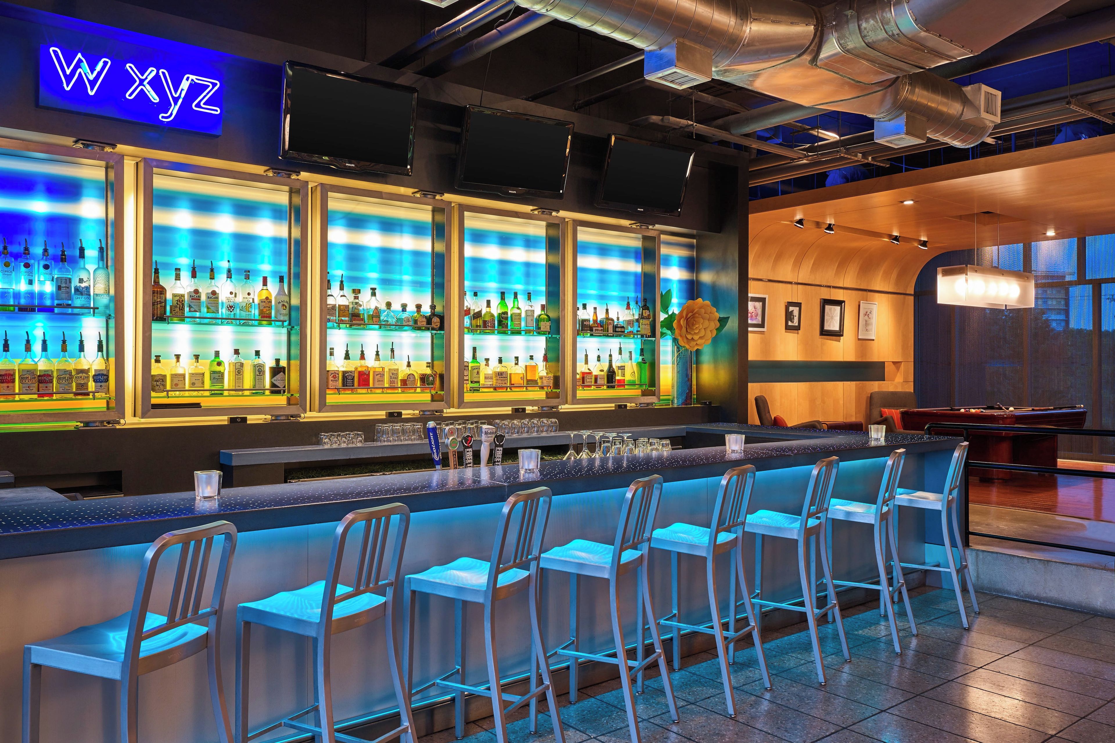 A bar area with multiple liquor bottles, a neon sign, and bar stools.