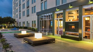 Un espace extérieur aménagé avec des canapés et des tables, un foyer et un bâtiment doté de grandes fenêtres et d’une porte en verre.
