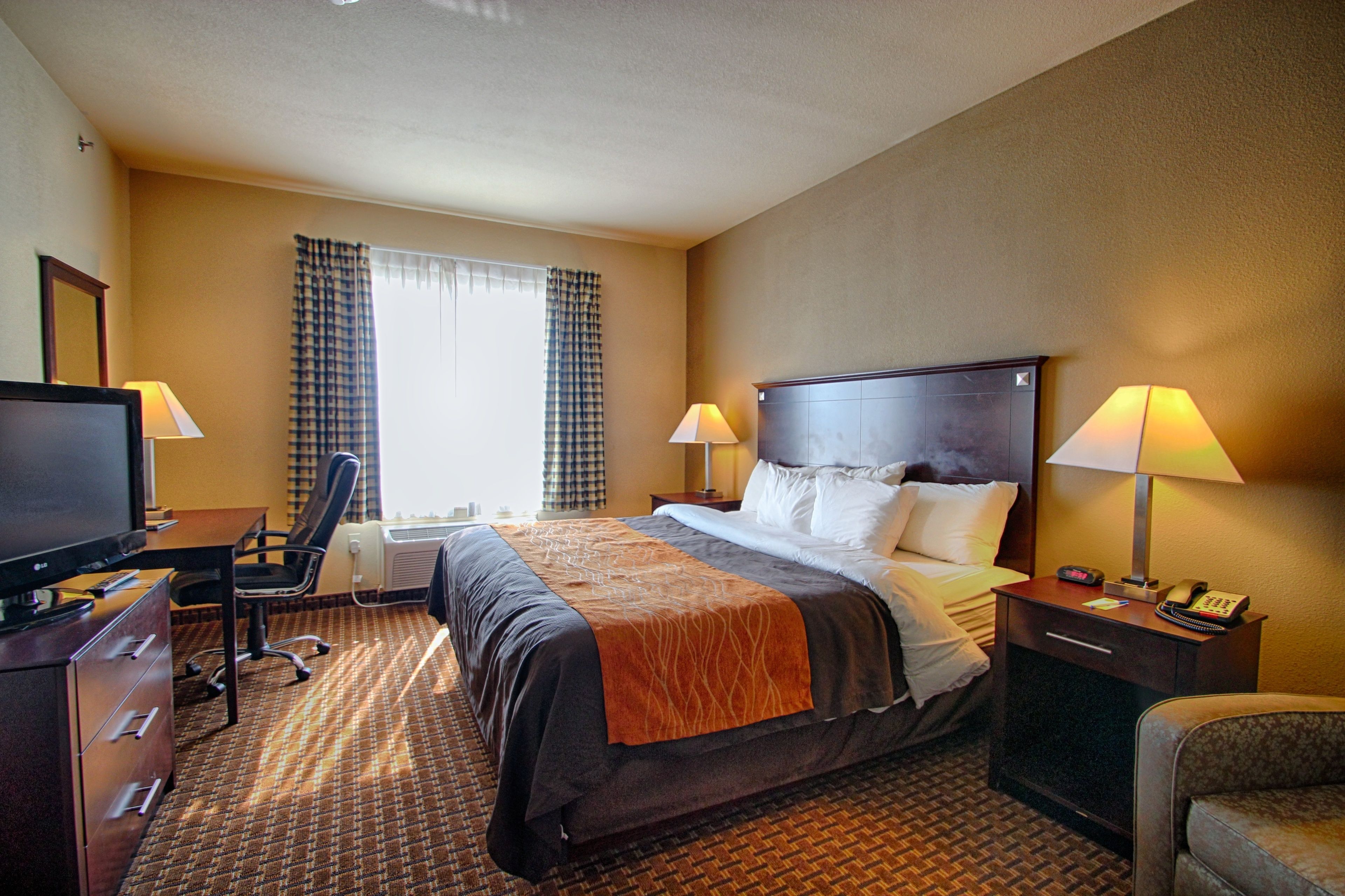 A hotel room with a bed, two bedside tables with lamps, a desk with a computer, a chair, and a television.