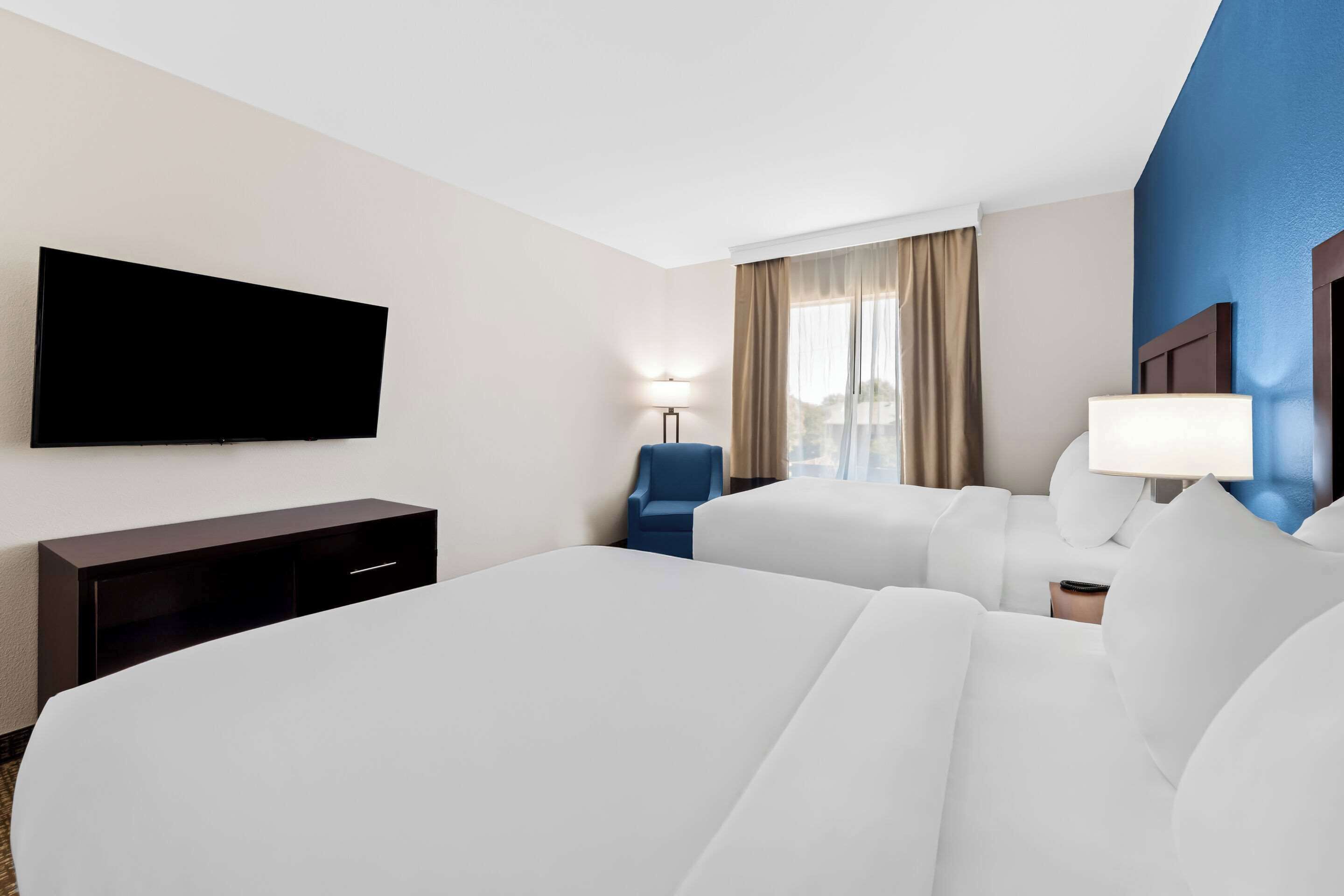 A hotel room with two beds, a flat-screen TV, a desk, a chair, and a lamp.