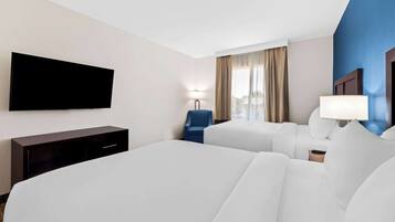 A hotel room with two beds, a flat-screen TV, a desk, a chair, and a lamp.