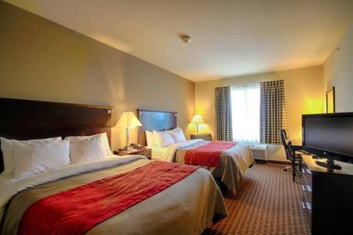 A hotel room with two beds, a desk, a television, and a window with curtains.