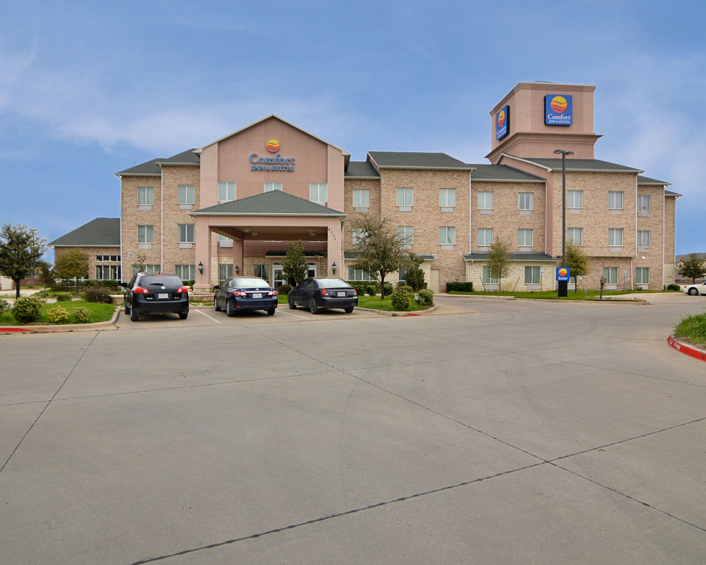 A Comfort Inn & Suites hotel with a brick facade, a covered entrance, and a parking lot with several cars.