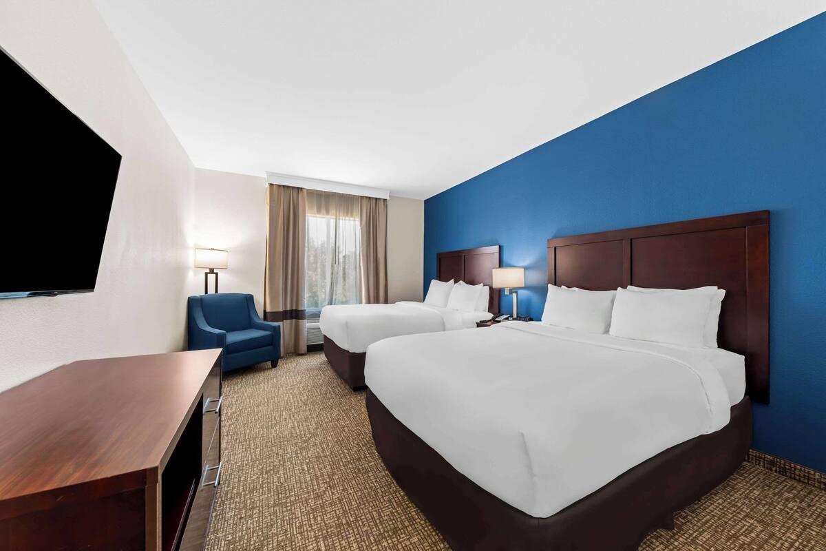 Ein Hotelzimmer mit zwei Betten, einem Schreibtisch, einem Sessel, einem Fernseher und einem Fenster mit Vorhängen.