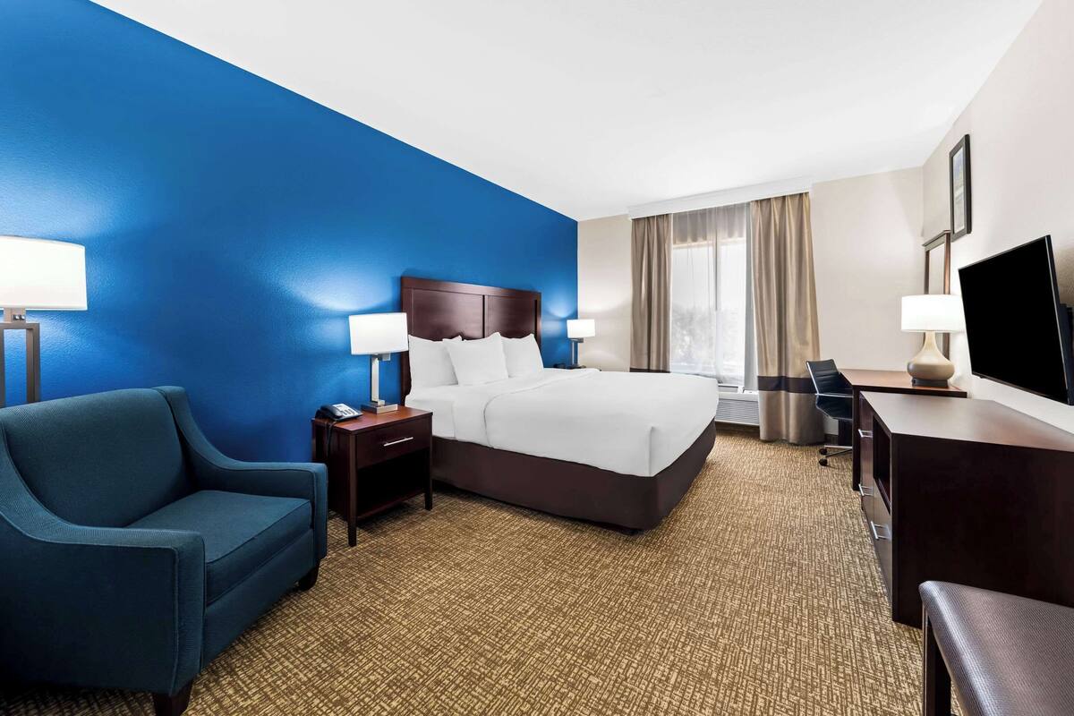 Ein Hotelzimmer mit einem großen Bett, einem Schreibtisch, einem Sessel und einem Fernseher.