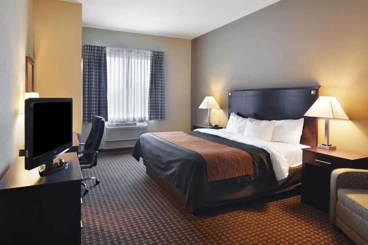Ein Hotelzimmer mit einem Bett, zwei Nachttischlampen, einem Fernseher, einem Schreibtisch und einem Sessel.