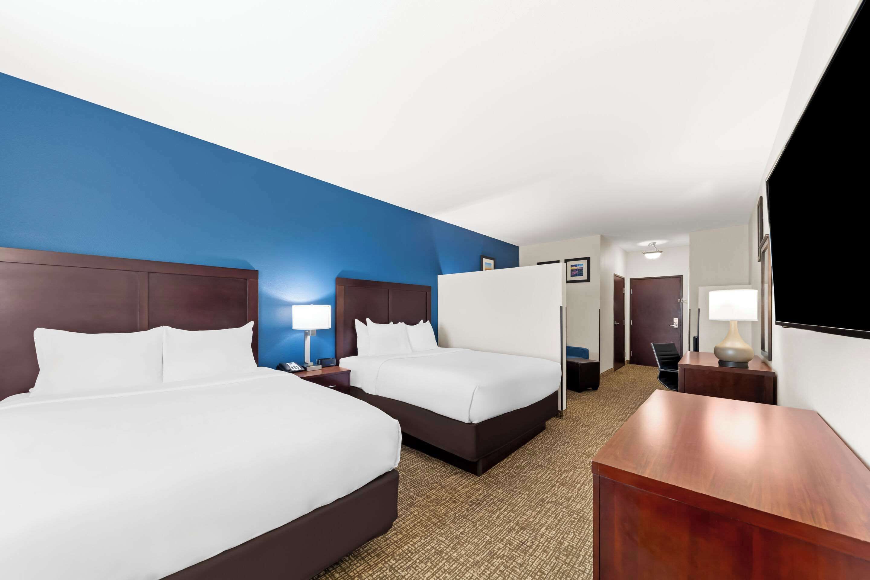 A hotel room with two beds, a desk, a chair, a lamp, and a mirror.