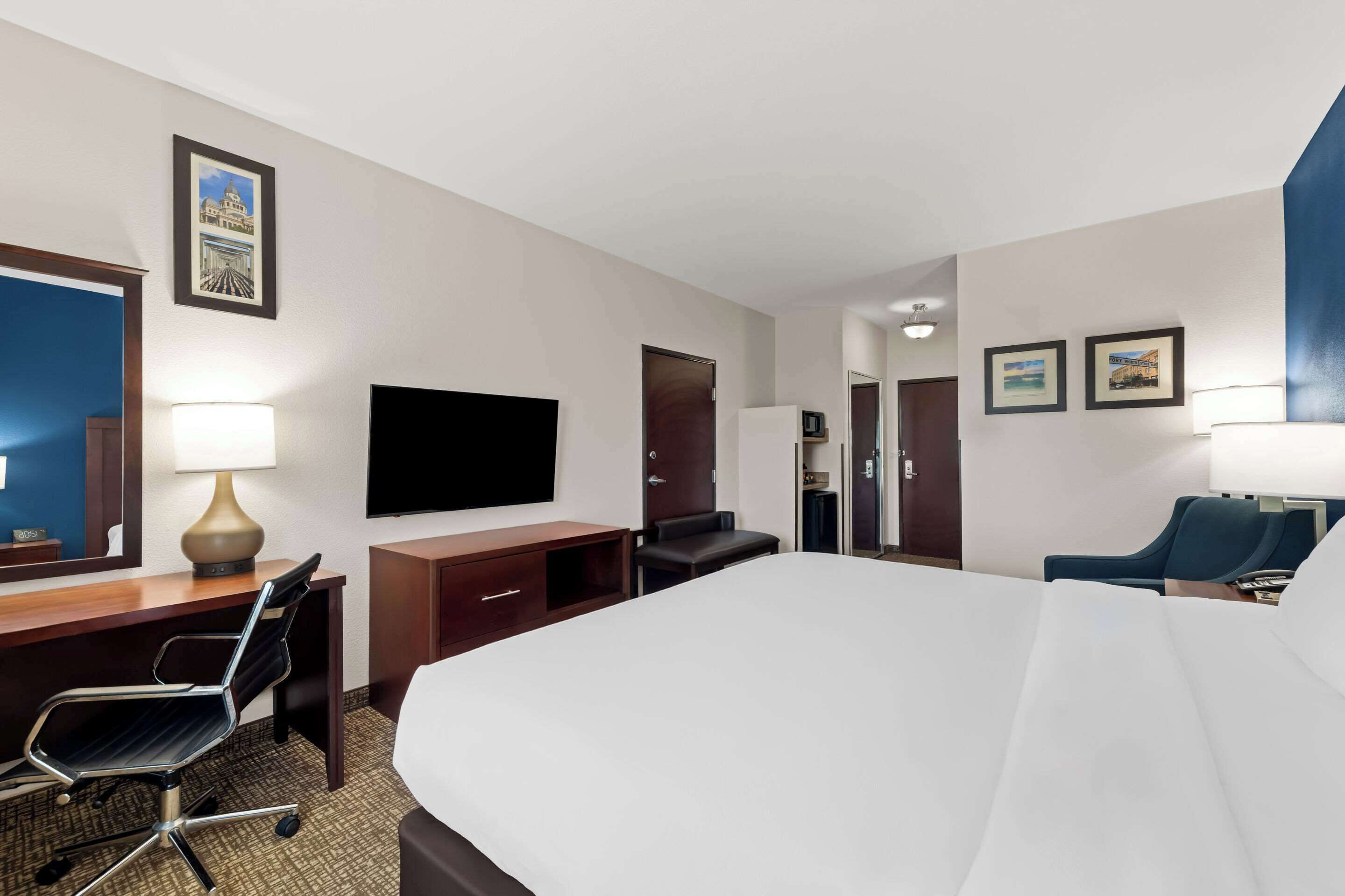 A hotel room with a large bed, a desk with a chair, a flat-screen TV, a desk lamp, and framed pictures on the wall.