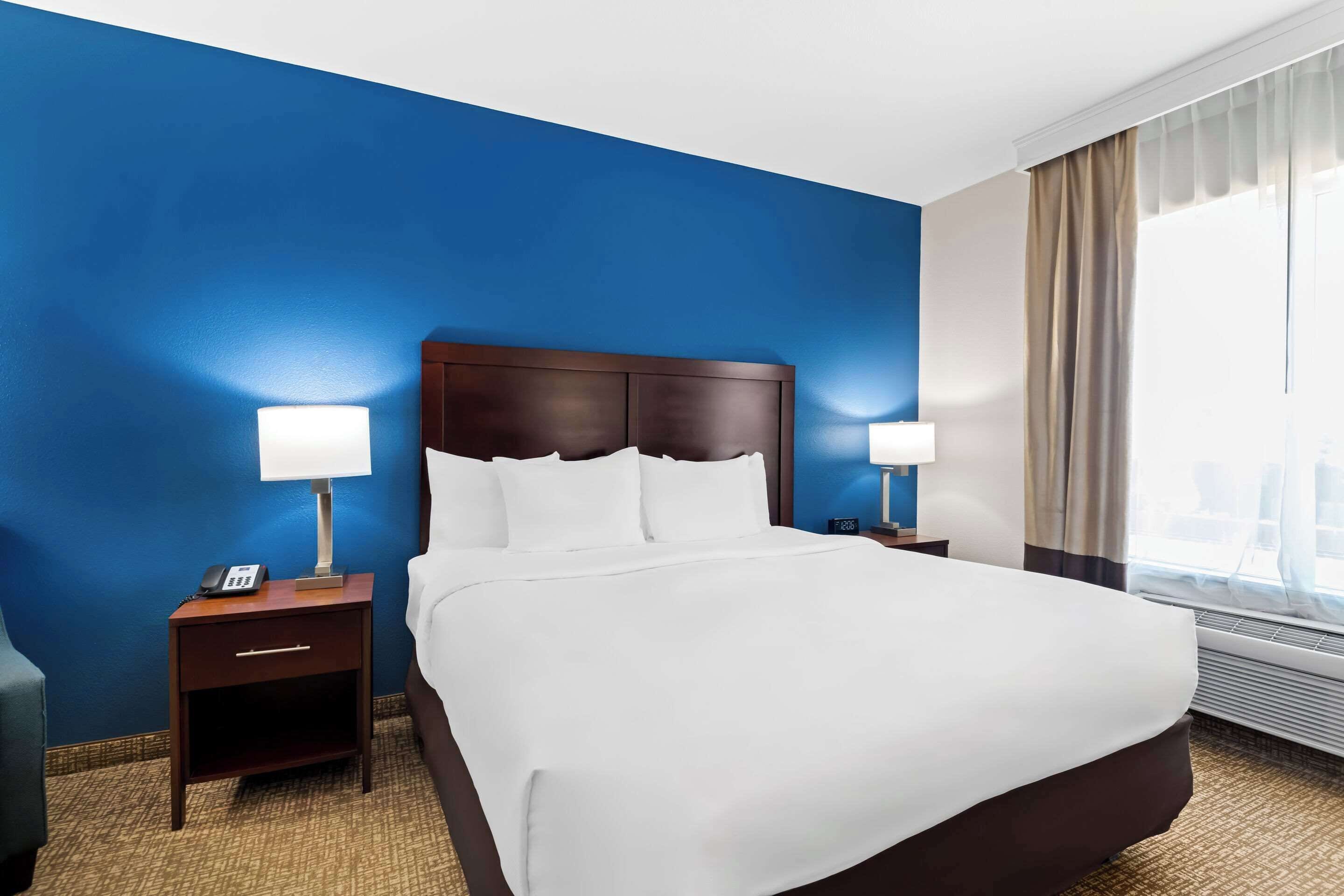 A hotel room with a large bed, two bedside tables with lamps, a phone, and a window with curtains.