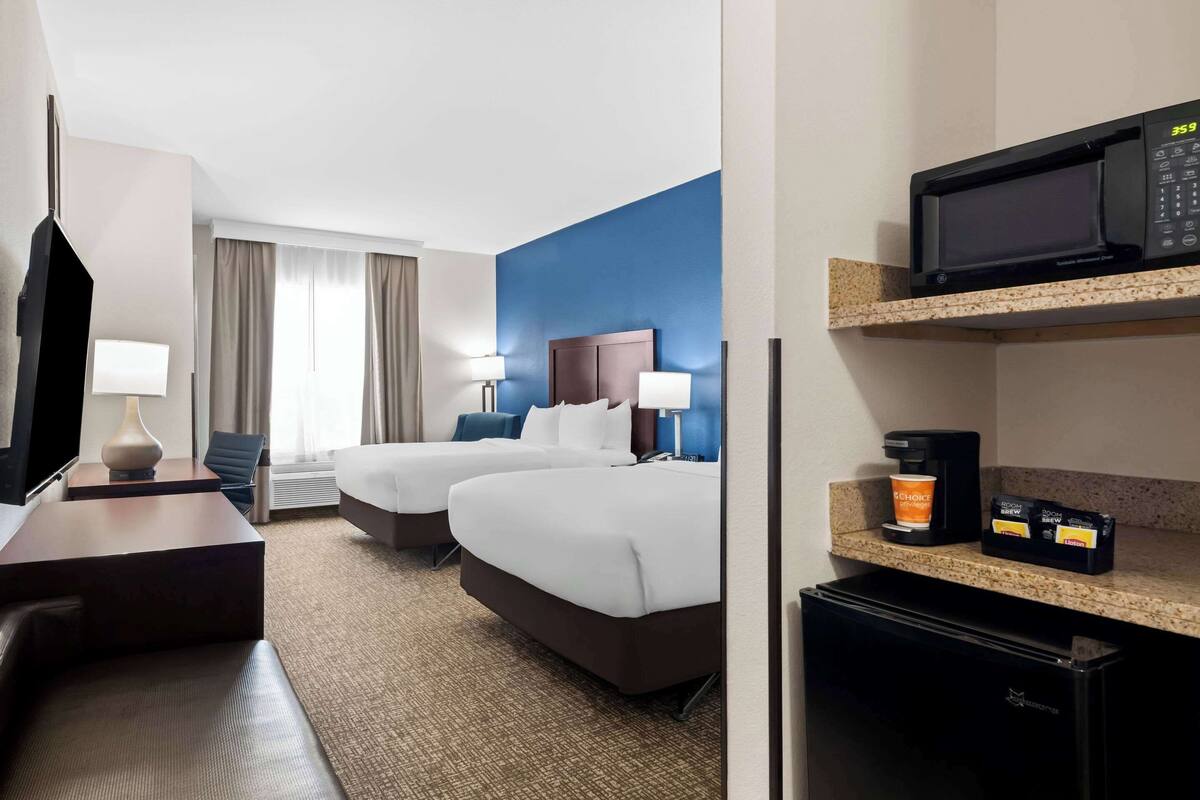 Ein Hotelzimmer mit zwei Betten, einem Schreibtisch, einer Mikrowelle, einer Kaffeemaschine und einer Minibar.