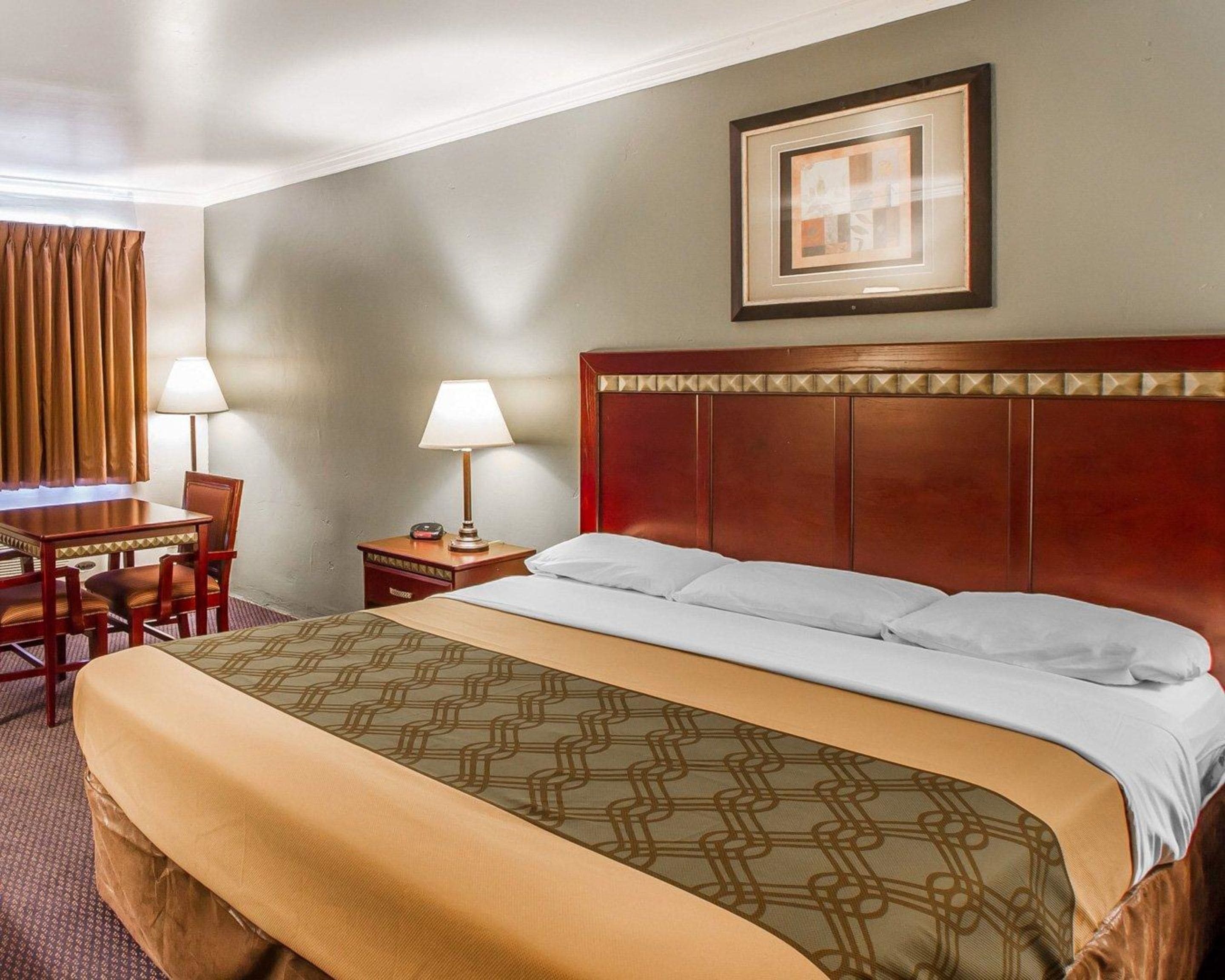 Una habitación de hotel con una cama grande, un escritorio con silla, dos lámparas de noche y un cuadro en la pared.