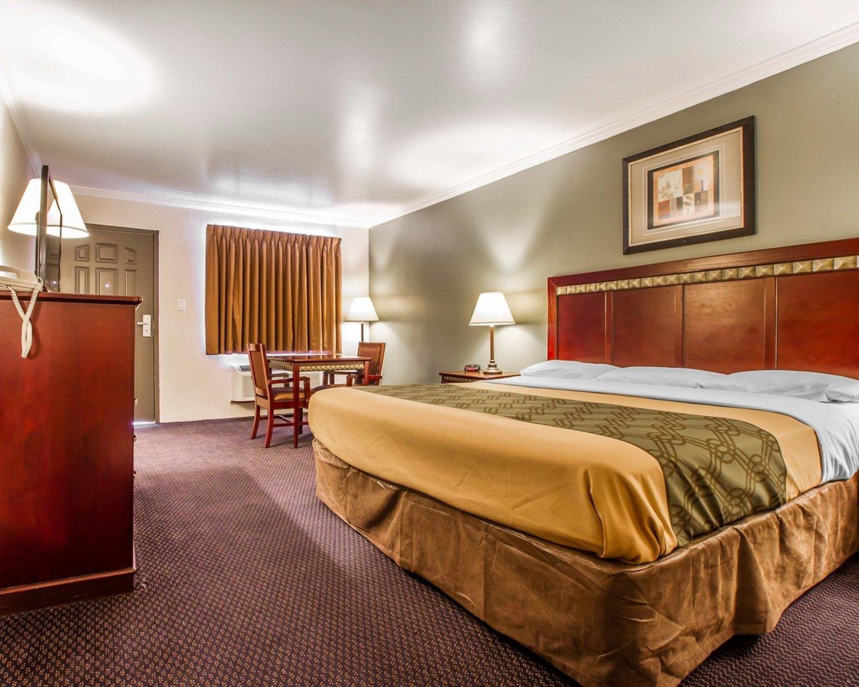 A hotel room with a large bed, a desk with two chairs, a telephone, and a picture on the wall.