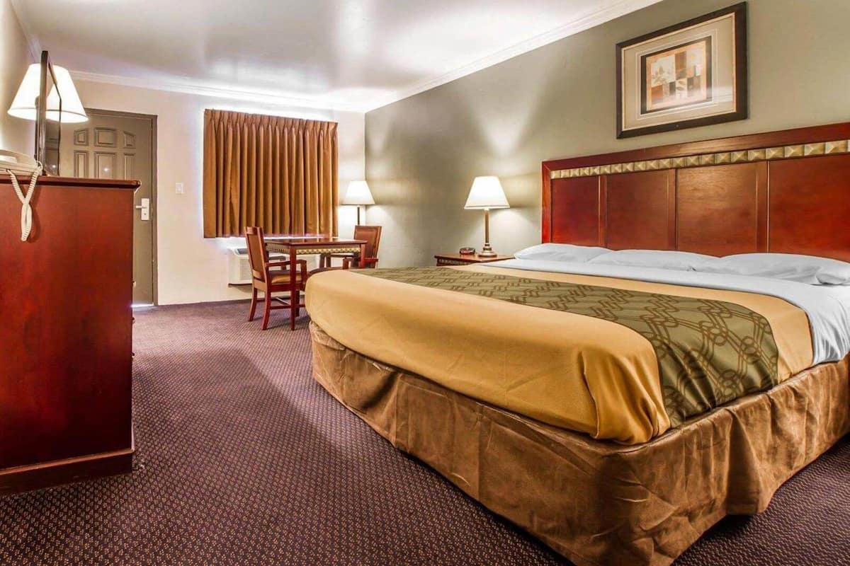 A hotel room with a bed, a desk, two lamps, a dresser, and a framed picture on the wall.