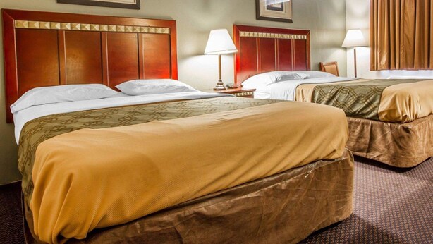 A hotel room with two beds, each with a wooden headboard, a bedside table with a lamp, and a framed picture on the wall.