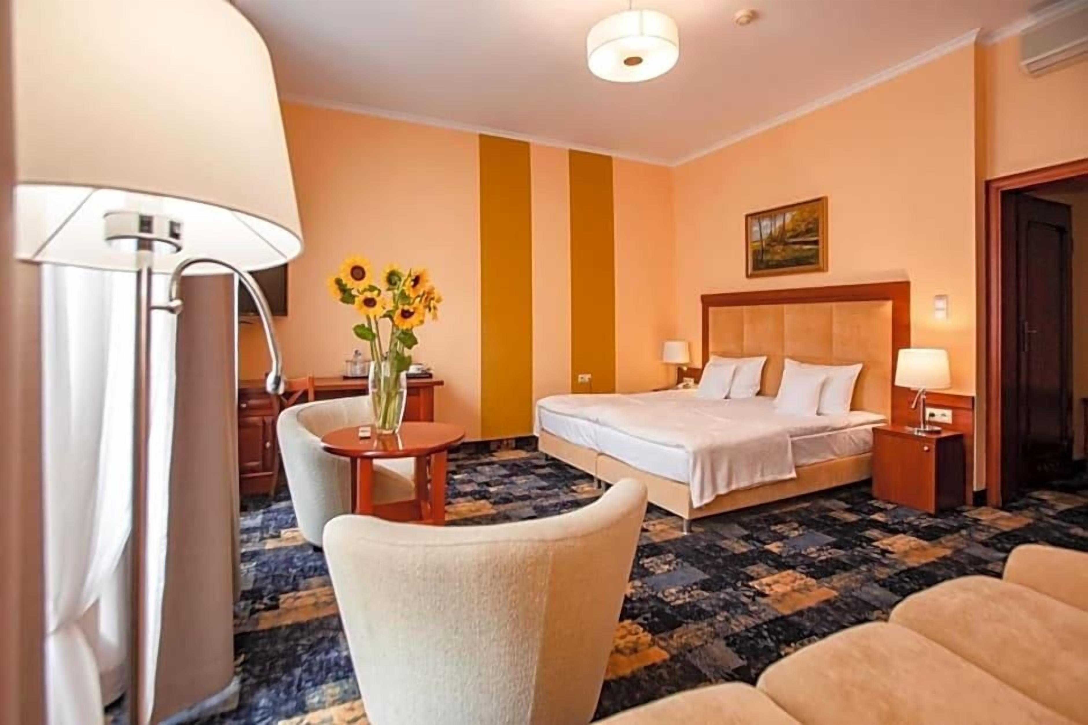 A hotel room with a bed, bedside tables, a lamp, a chair, and a vase with sunflowers.